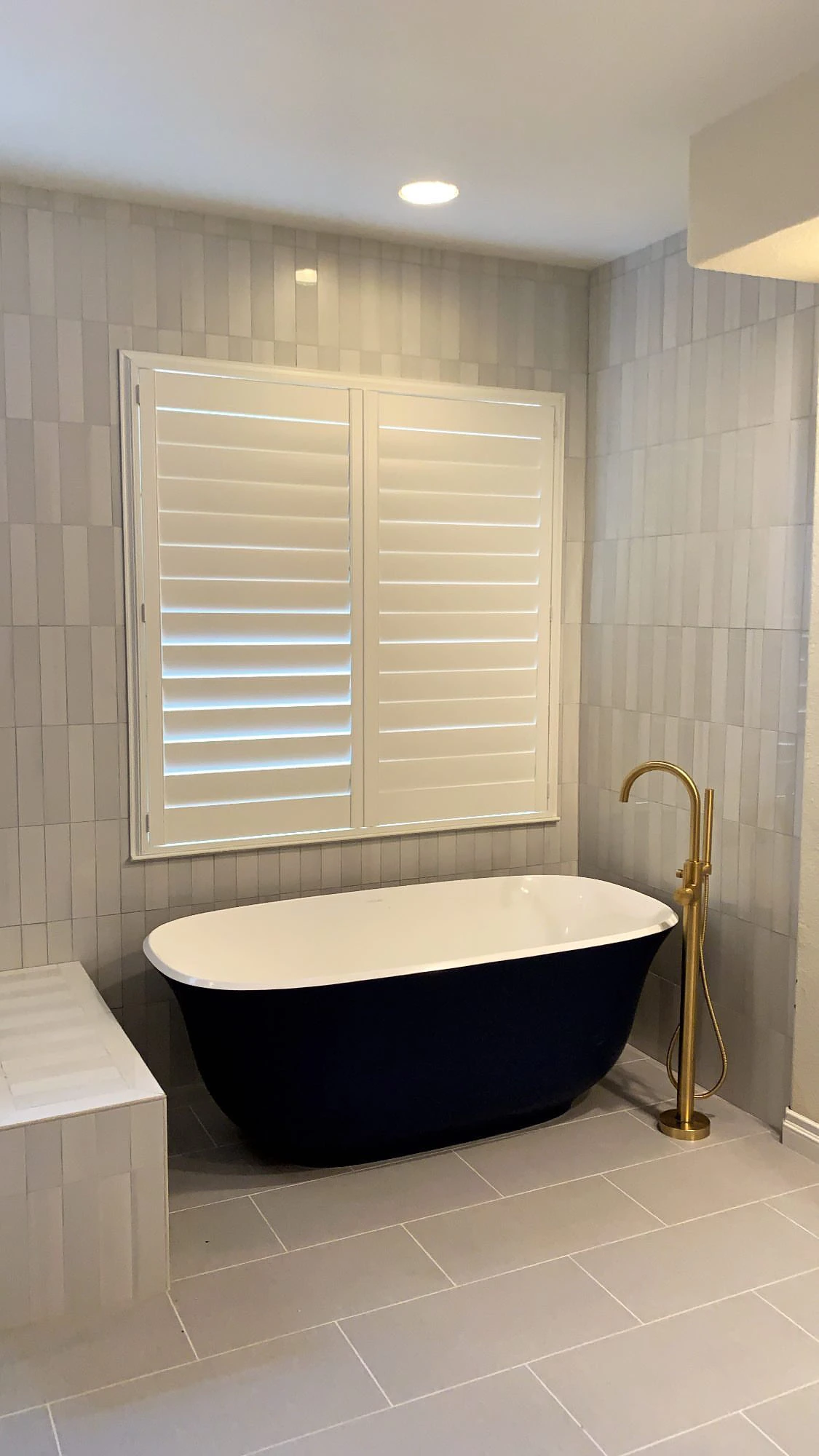 Freestanding black tub with floor-mounted brass filler and full-height tile